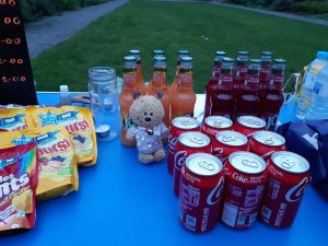 A blue table at dusk, outside on grass bearing sweets, soft drinks - all of which are vegan